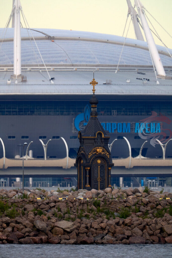 Маленькая черная часовня с золотыми элементами на фоне стадиона «Газпром Арена»